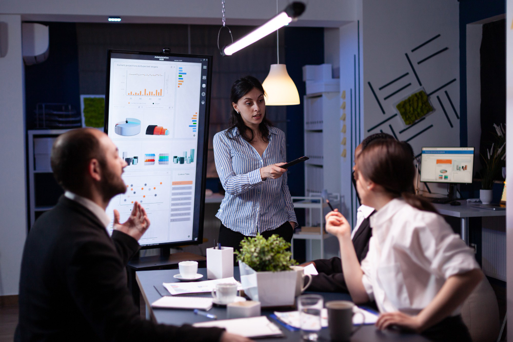 A woman presenting data to colleagues in a meeting room, symbolizing teamwork and communication.